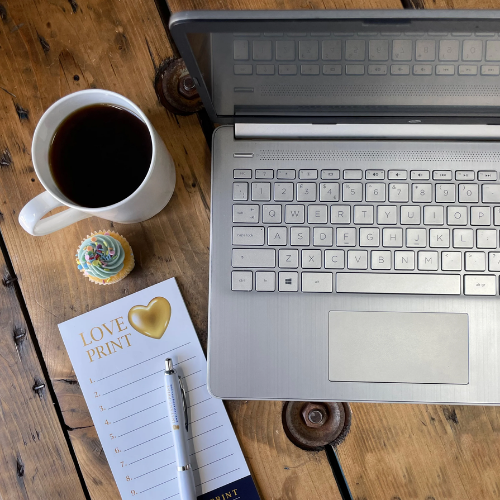 Open laptop on a wooden table with a cup of coffee, notebook, and pen.