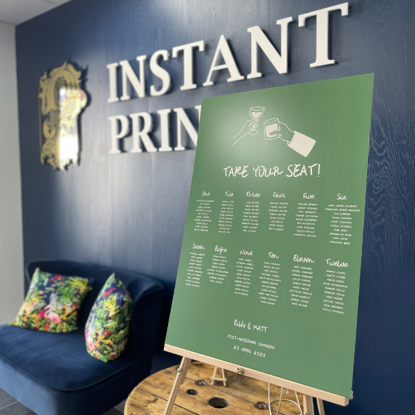 Green seating chart on an easel against a blue wall with 'Instant Print' sign.