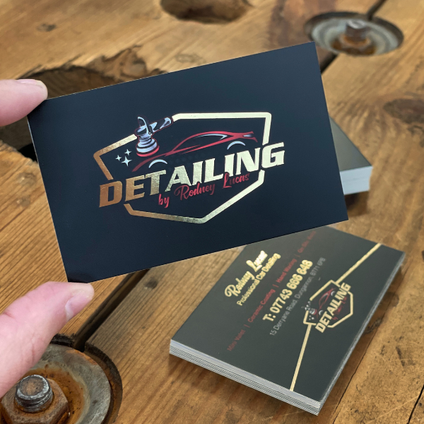 Black business cards with gold foiling held over a wooden table