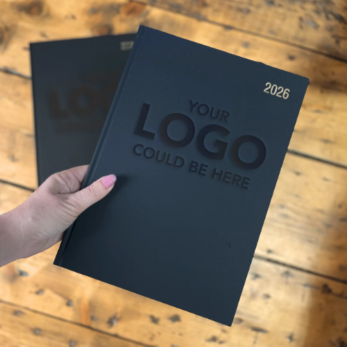 Black diary with 'Your logo could be here' text held by a hand on a wooden surface