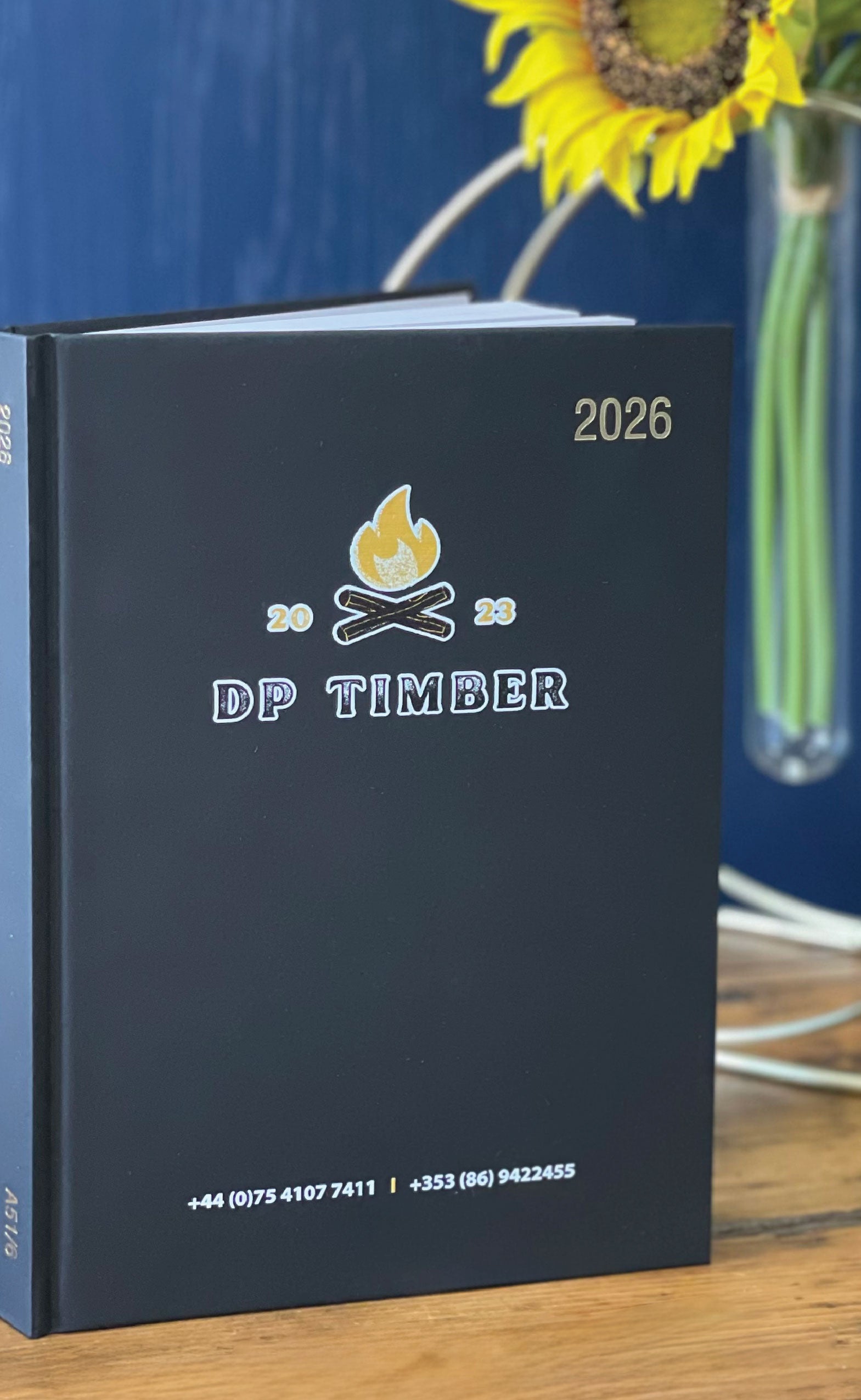 Black 2026 Branded diary DP Timber branding on a wooden surface with a sunflower in the background.