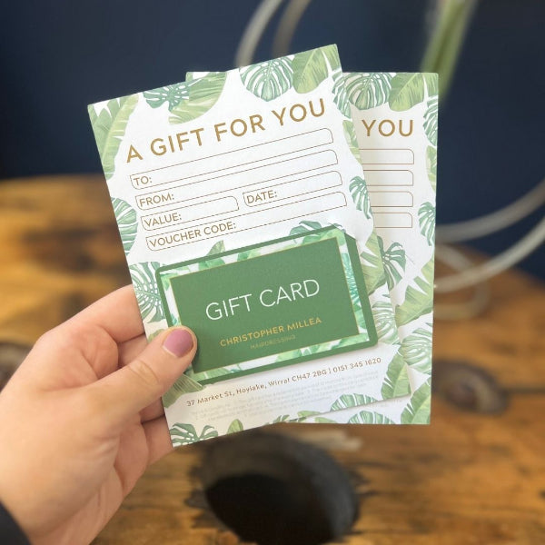 Hand holding a gift card holder with tropical leaf design and a UV Printed Gift Card on a wooden surface