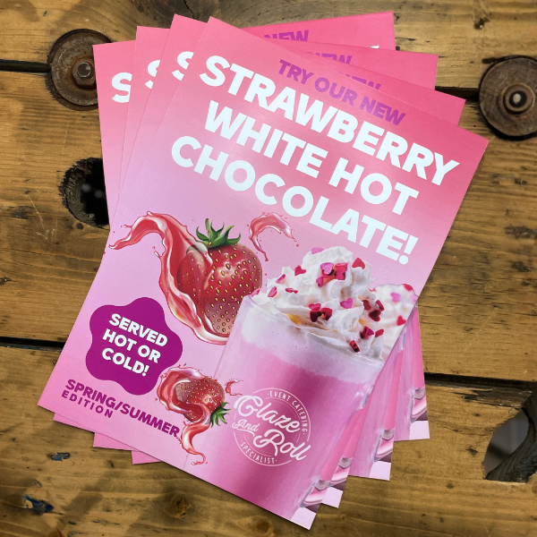stack of pink milkshake promotion posters on wooden table