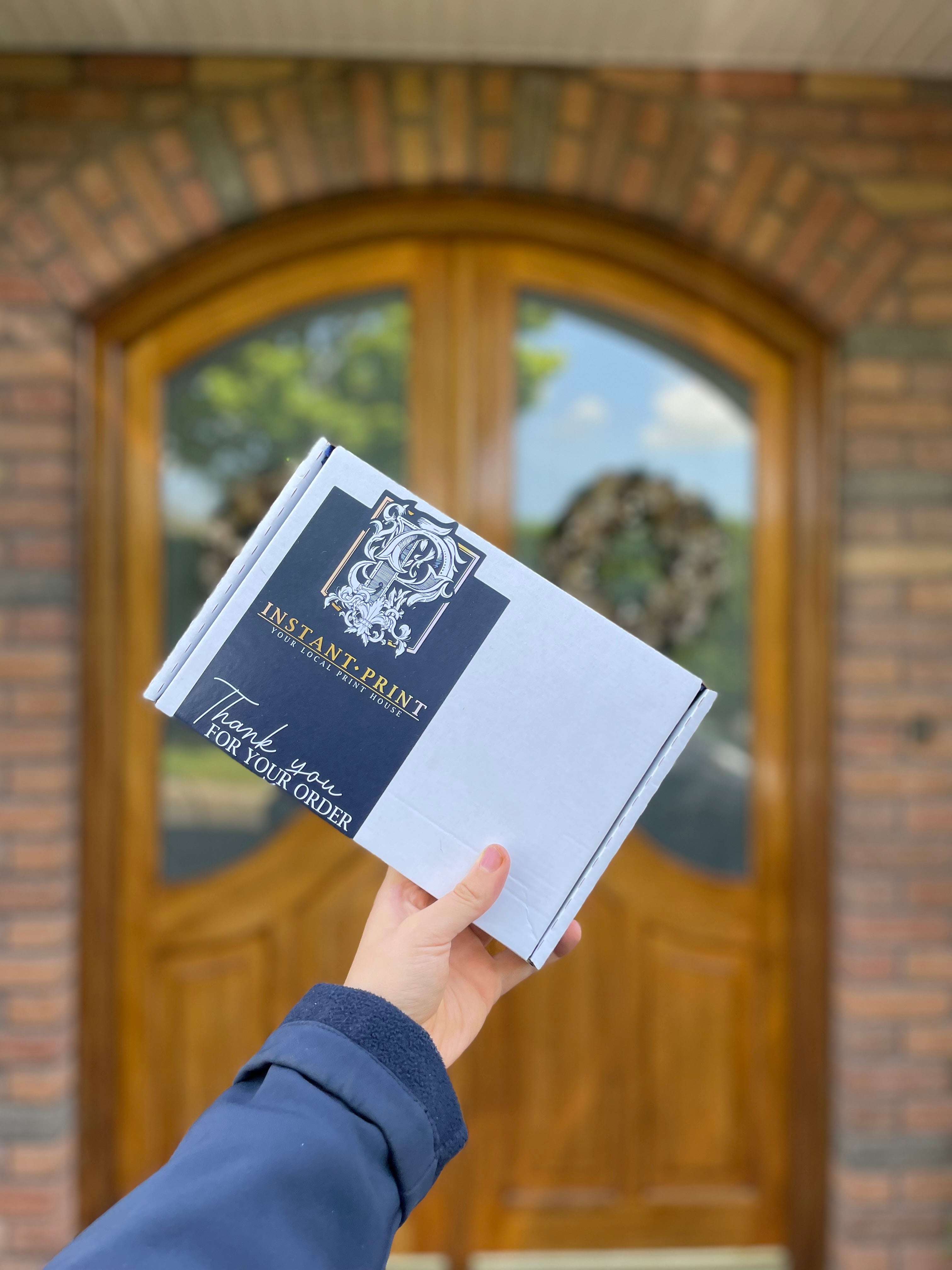 Person holding an 'Instant Print' box in front of a brick building with a glass door.