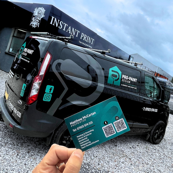 Black van with branding and a hand holding a business card in front.