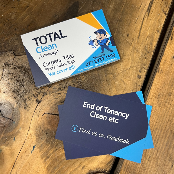 Two business cards on a wooden surface, one for 'Total Clean Armagh' and the other for 'End of Tenancy Clean etc'.