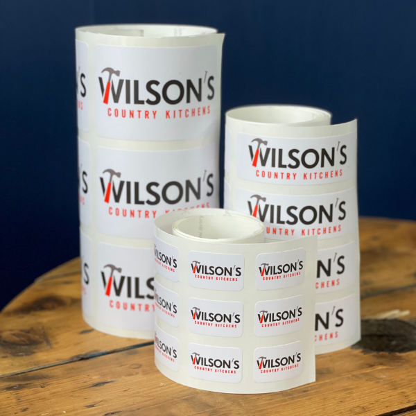Rolls of stickers with 'Wilson's Country Kitchens' branding on a wooden surface.