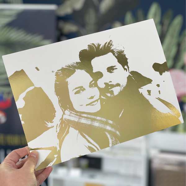 Gold and white portrait on a card held by a hand with a blurred background