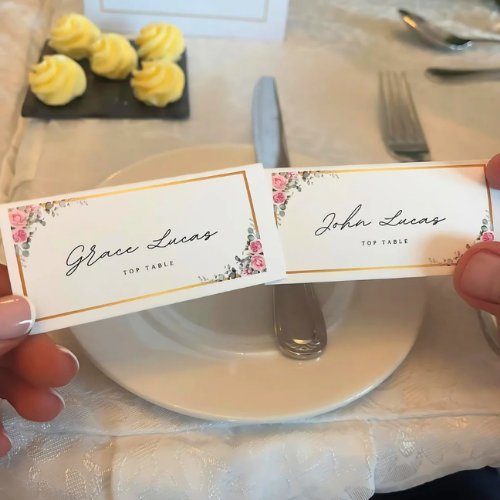 Two place cards with floral designs held over a set table.
