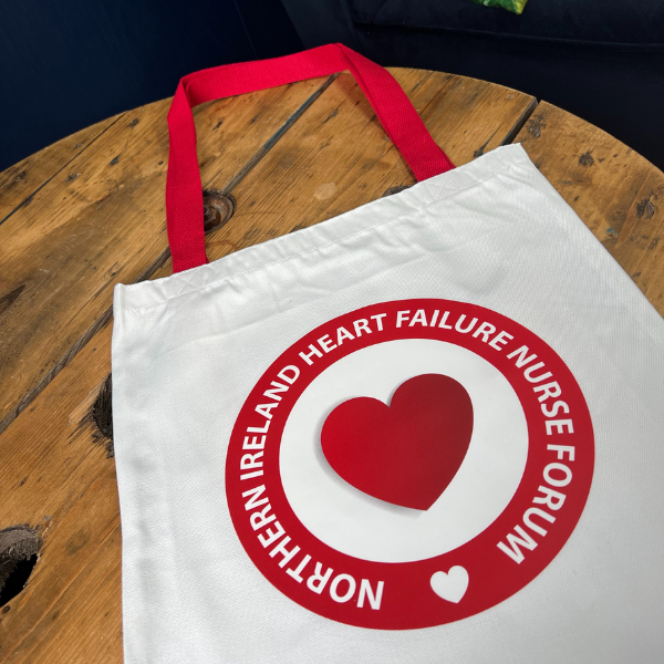 White tote bag with red heart and text on a wooden surface