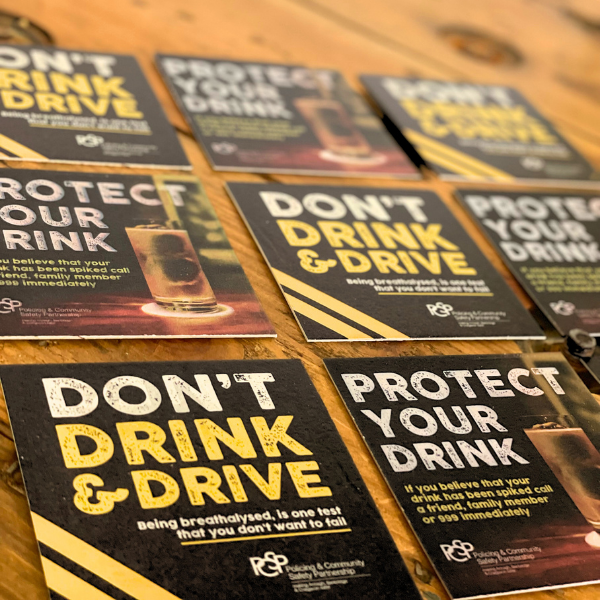 Collection of 'Don't Drink & Drive' and 'Protect Your Drink' printed beer filts on a wooden surface.