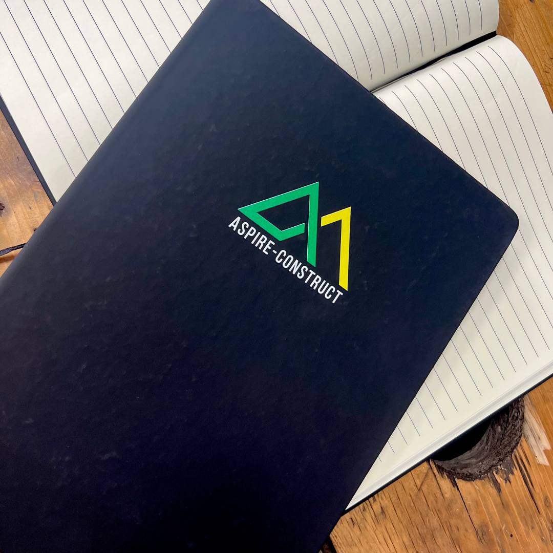 Black A4 Notebook with 'Aspire Construct' logo on a wooden surface