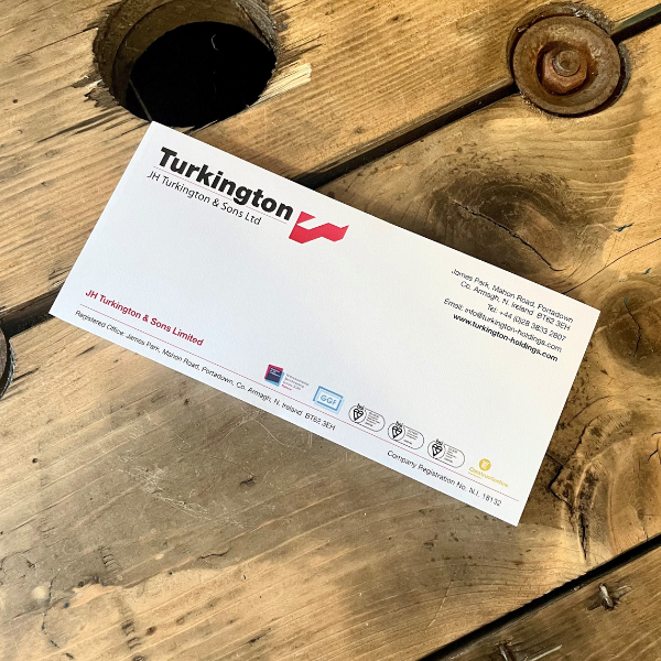 A white compliment slip with a company's details printed on it, lying on a wooden surface.