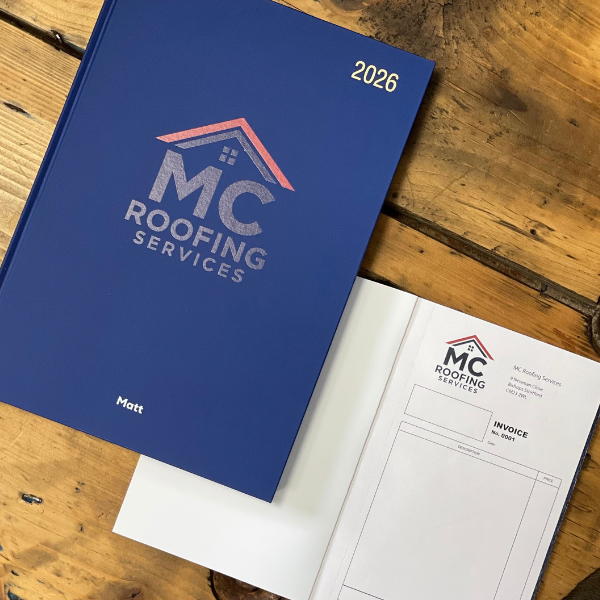 Navy 2026 Diary with MC Roofing Services branding on a wooden surface and matching invoice book