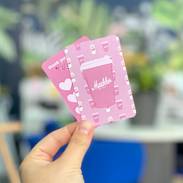 Pink loyalty cards with a coffee cup design held by a hand against a blurred outdoor background.