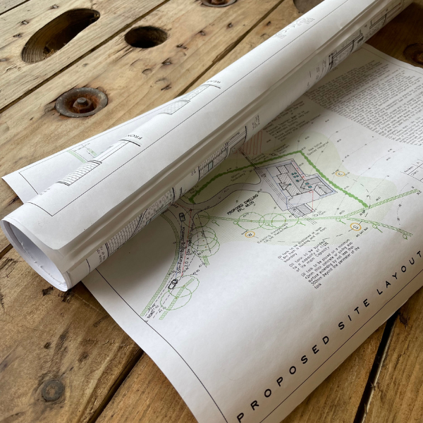A rolled-up architectural plan print laying on a wooden surface, with visible details of a building layout.