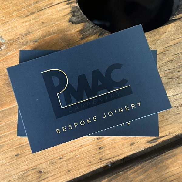 Blue business card with 'PMAC Carpentry Bespoke Joinery' on a wooden surface