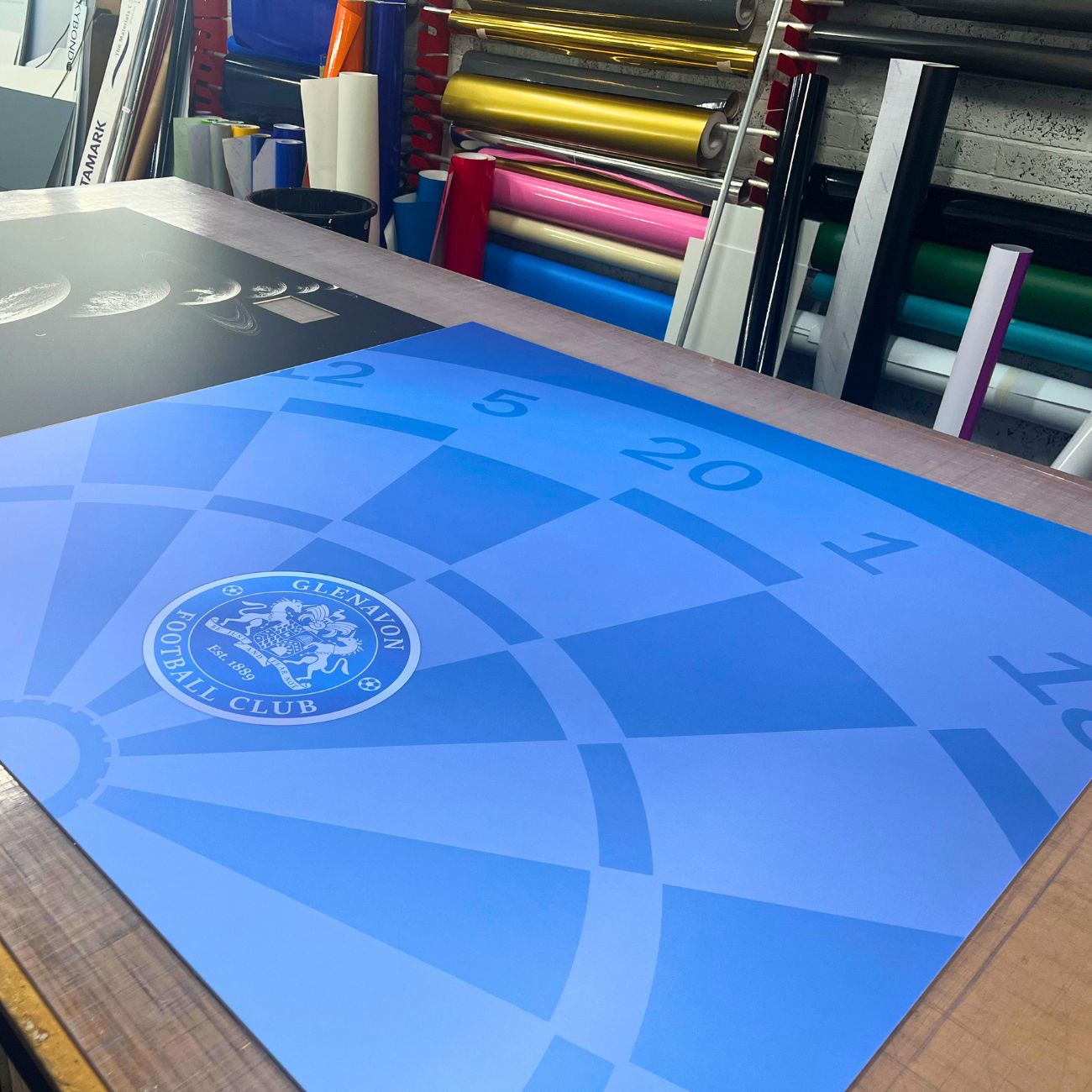 Blue graphic on a protective rigid Backdrop with a logo on a table in the Instant Print studio
