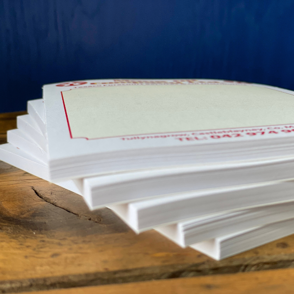Stack of white note pads with red text on a wooden surface against a blue background