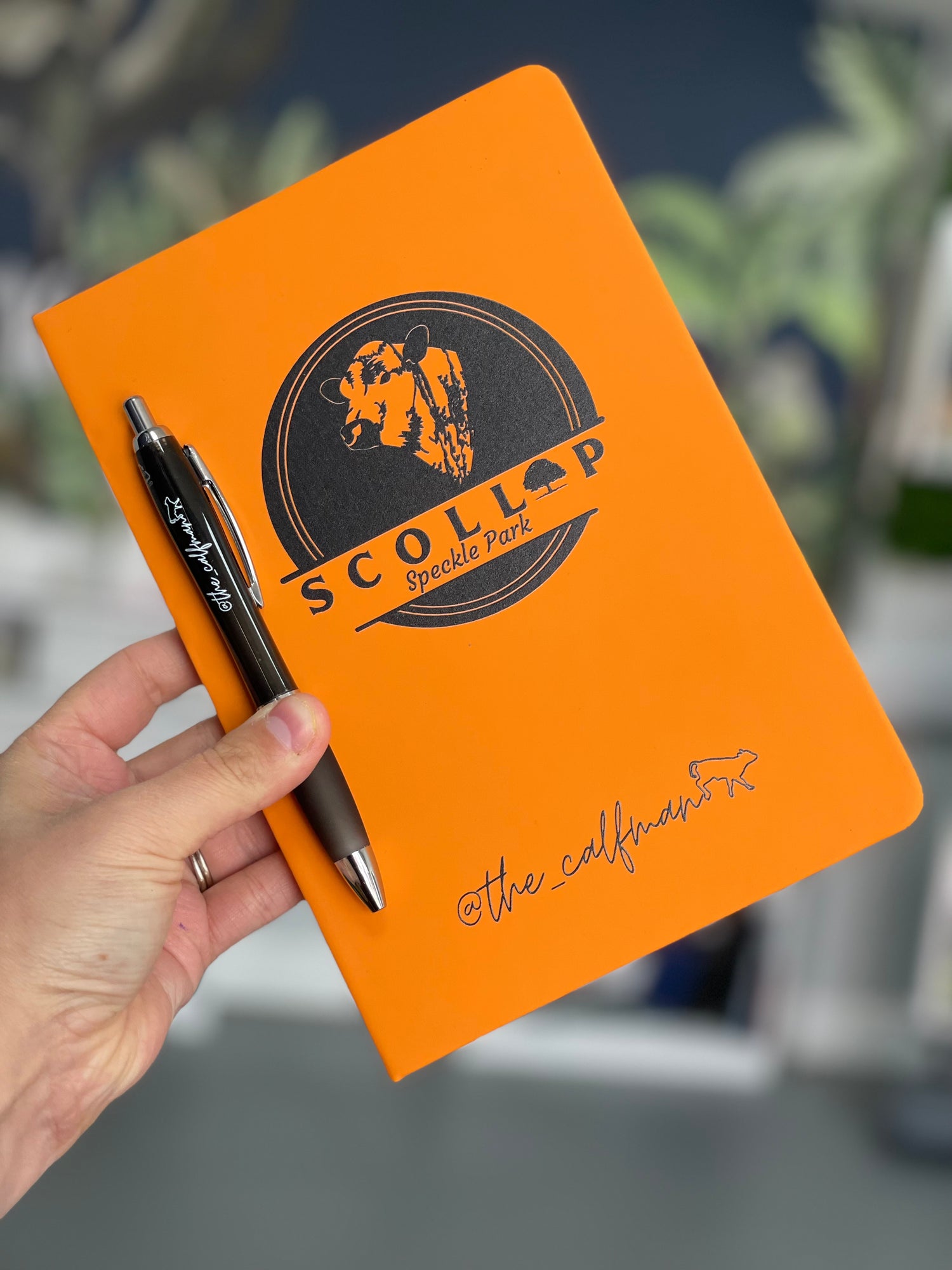 Orange notebook with a logo and pen held by a hand against a blurred background
