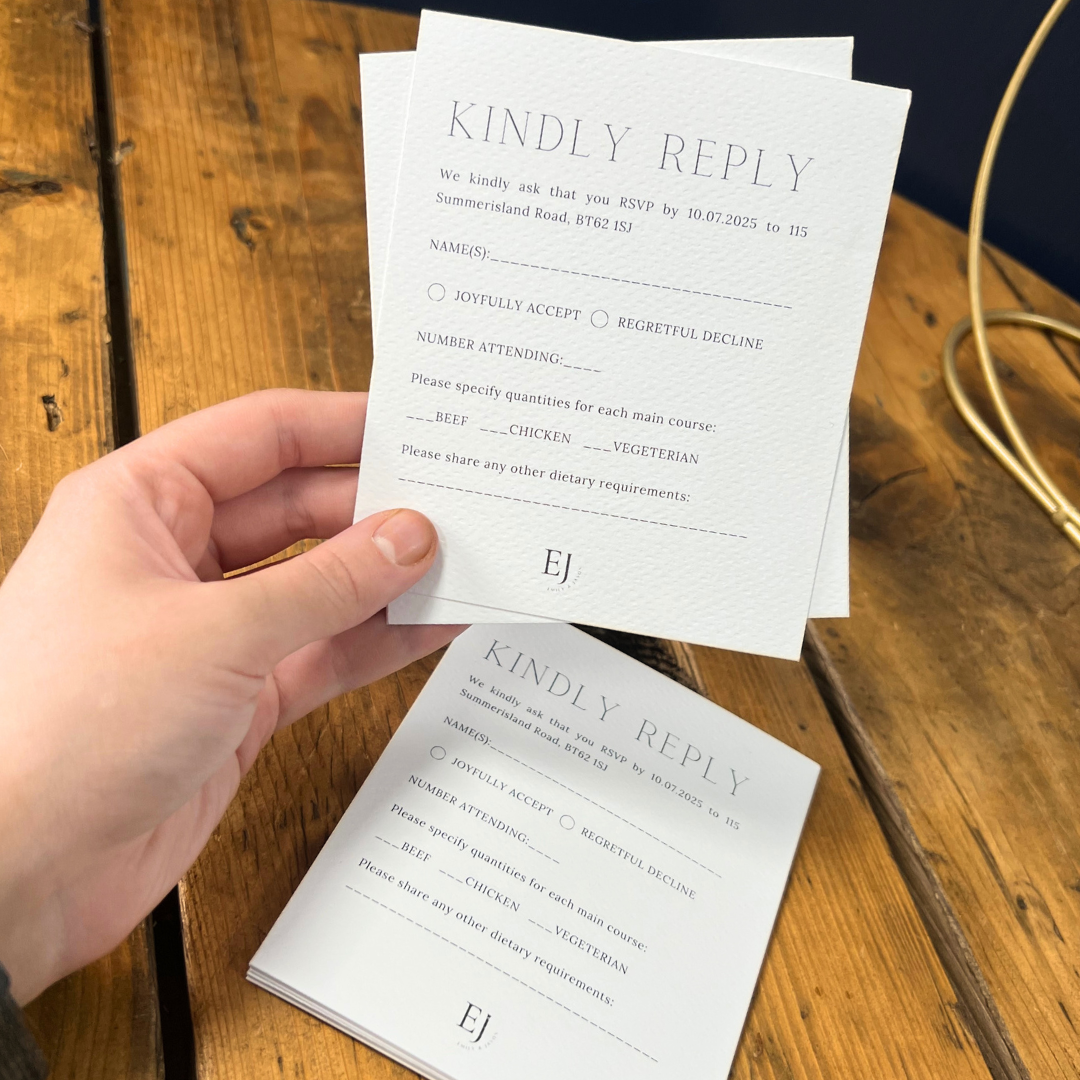 Hand holding a set of wedding invitation reply cards on a wooden surface