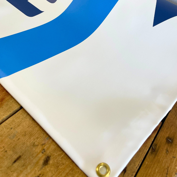 Close-up of a blue and white sign with a gold eyelet on a wooden surface