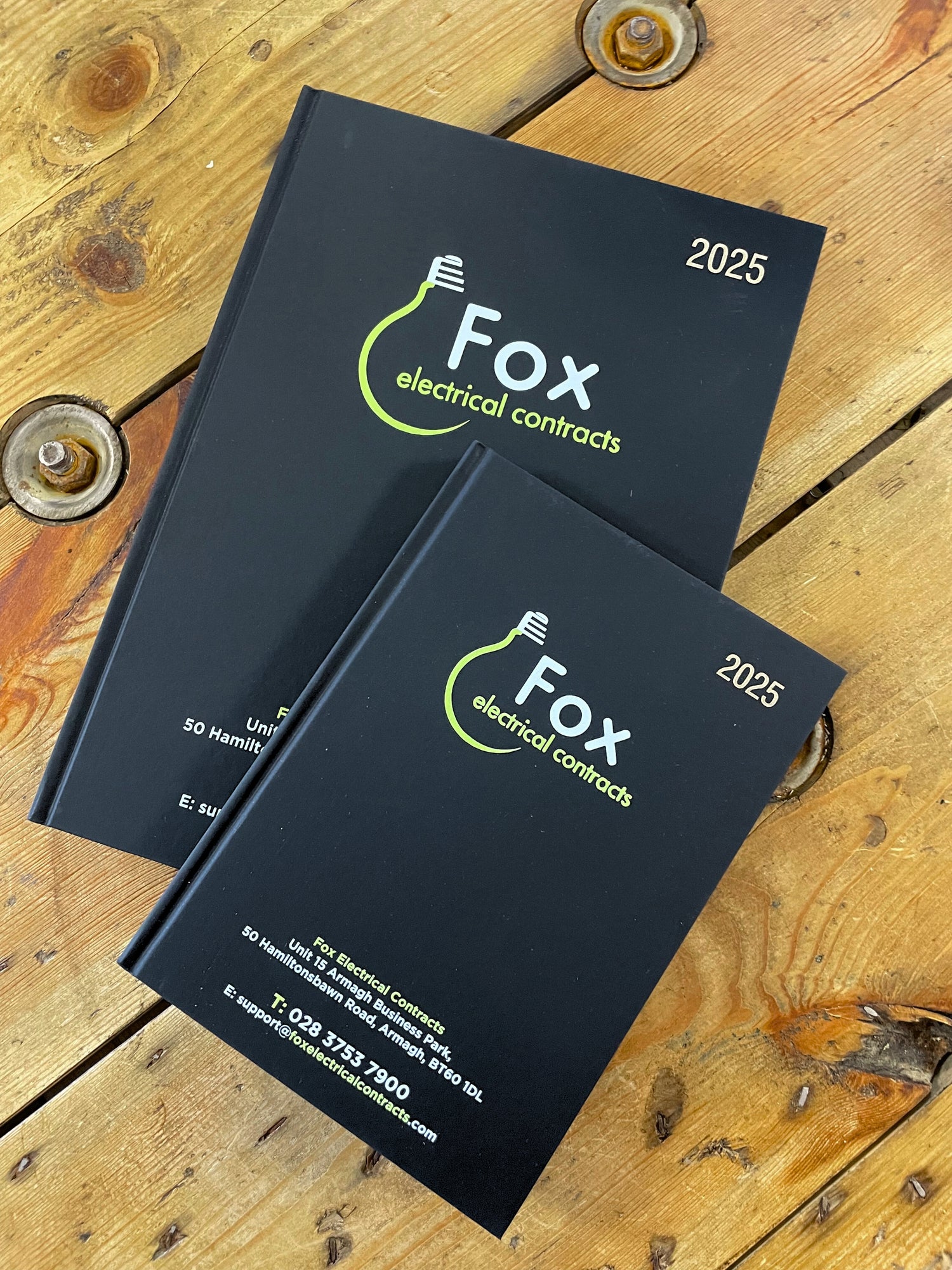 Two diaries 2025 with 'Fox electrical contracts' branding on a wooden surface.