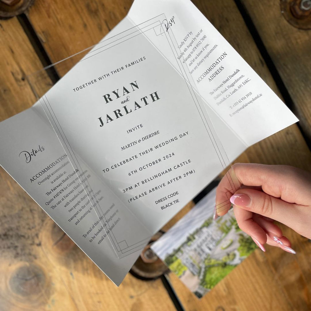 Acrylic Wedding Invitation being taken out of a black envelop and displayed on a wooden table.