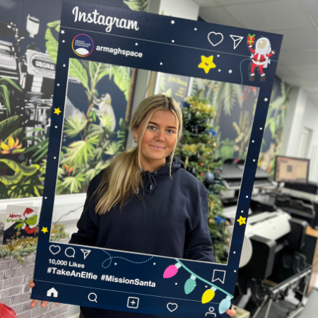 Person holding a festive Instagram frame with holiday-themed icons in an office setting.